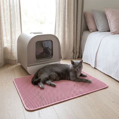 Tapis litière chat rose avec un chat gris couché devant son bac dans une chambre lumineuse.