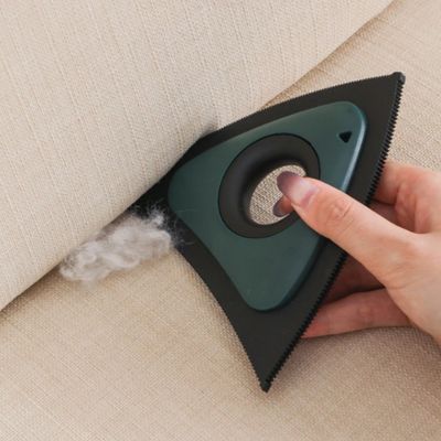 brosse anti poil triangulaire verte et noire retirant des poils dans le creux d’un canapé beige