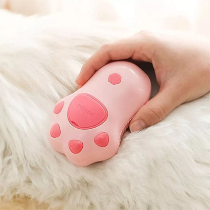 Brosse pour chat rose tenue dans une main, avec un motif de coussinets et un bouton sur le dessus.