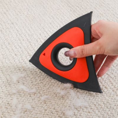 brosse anti poil triangulaire orange et noire utilisée à la main sur un tapis beige