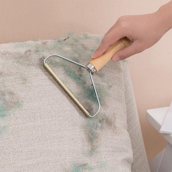 Brosse anti-poil à manche en bois retirant des peluches sur un tissu beige