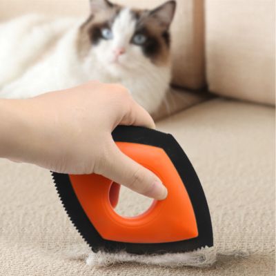 brosse anti poil orange et noire rassemblant des poils sur un canapé beige, avec un chat en arrière-plan