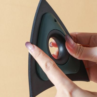 brosse anti poil triangulaire verte et noire tenue en main, avec un doigt montrant sa bordure dentelée