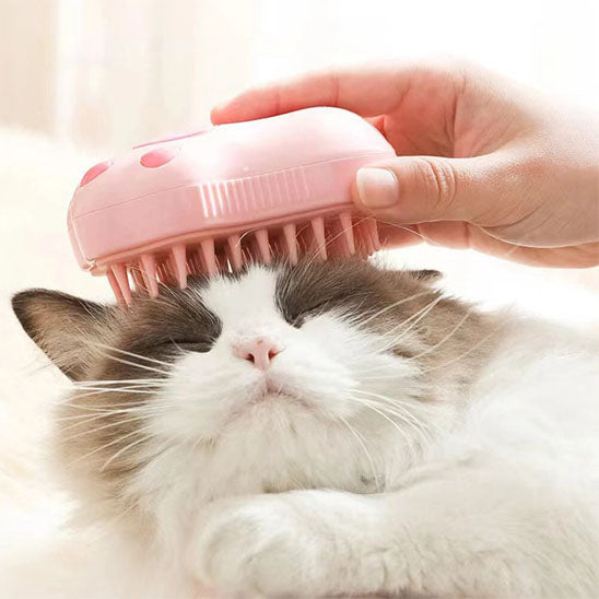 Brosse pour chat rose utilisée sur le haut de la tête d’un chat blanc et gris aux yeux fermés.