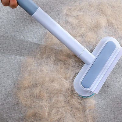 Brosse anti-poils à long manche retirant une accumulation de poils sur un tissu gris