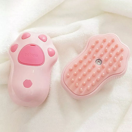 Brosse pour chat rose présentée recto verso sur un tissu blanc, avec ses picots et son ouverture centrale.